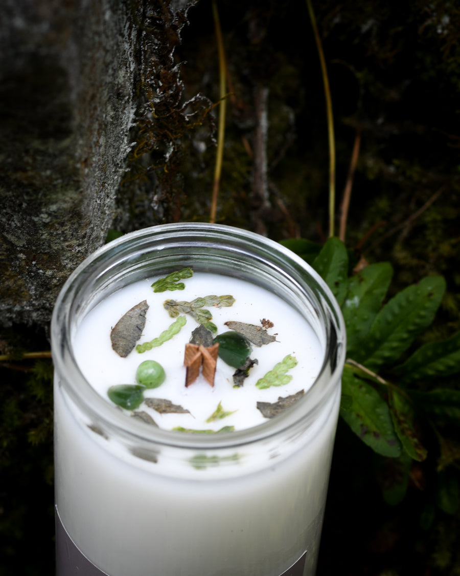Top View of an Abundance canle with peony flower petals and jade resting in moss