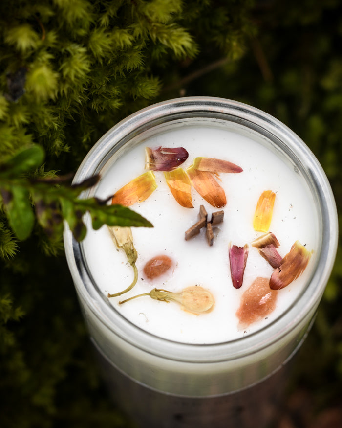 Top view of a Gratitude candle with flower petals and sunstone resting in moss