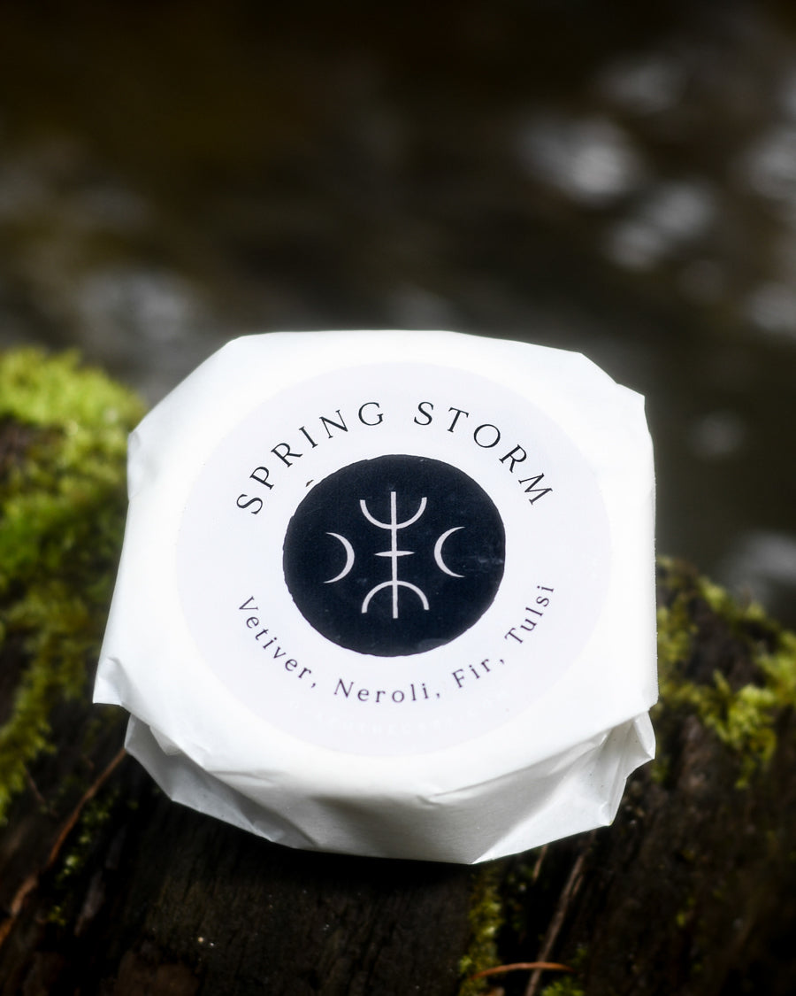 Spring Storm bath bomb with Vetiver, Neroli, Fir, Tulsi by O Apothecary resting by a creek on a mossy log