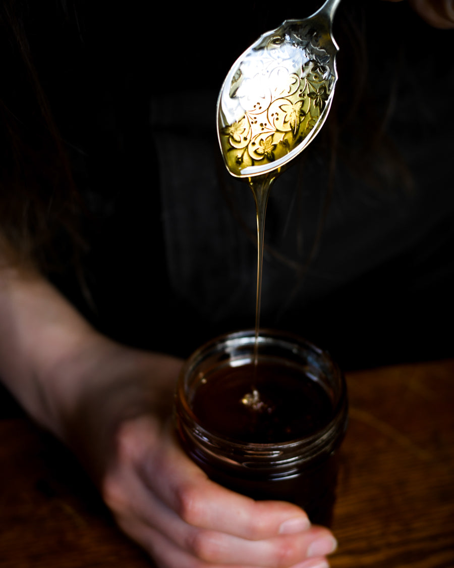 Raw honey regeneratively harvested being scooped out of a jar and drizzling off an antique spoon